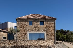 Rustic stone house with tiled roof and large windows.