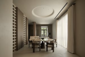 A modern residential dining room featuring a circular wooden table with marble top and matching chairs, surrounded by large w