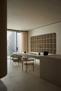 A minimalist interior space featuring concrete furniture and flooring, with a modern bookshelf and seating area by a large wi