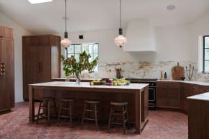 A modern kitchen with an island, wooden stools, marble countertops, and a large window.
