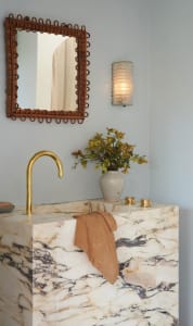 Modern bathroom with a marble countertop, brass faucet, and decorative vase with flowers.