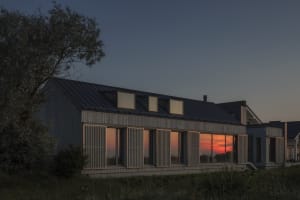 A modern house with metal cladding and large glass windows against a sunset sky.