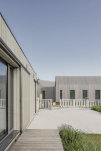 Modern residential exterior with wooden board and batten siding and a white picket fence.