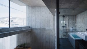 Modern minimalist bathroom with concrete walls and floor, featuring a glass-enclosed shower and sink.