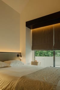 A minimalist bedroom with white walls, a textured fabric bedspread, and a window with dark blinds.
