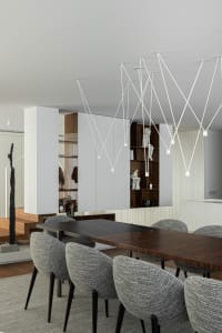Modern black dining table surrounded by grey upholstered chairs with a grey textured floor treatment.