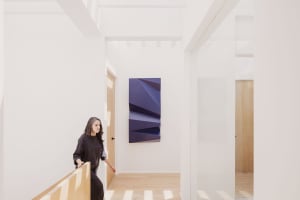 A minimalist interior space with a white wall, wooden floor, and modern artwork