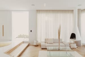 Modern minimalist living room with white furniture and curtains, glass coffee table, and tall vase with dried plants