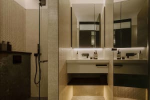 Modern bathroom with tiled walls, minimalist mirror, and metal dimmer switches.