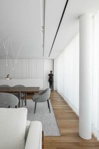 Modern minimalist living room with wood flooring, fabric furniture, and glass windows.