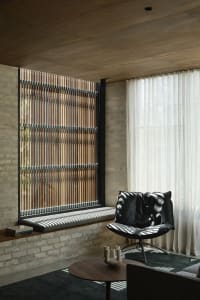 Modern living room with brick walls and wooden blinds, featuring a black lounge chair and coffee table.