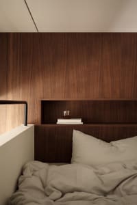 A modern minimalist bedroom featuring a wooden storage unit with books and a glass