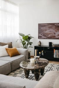 A modern living room with a gray sectional sofa adorned with decorative pillows, a round marble coffee table, and a dark book