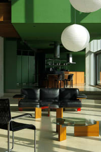 A modern living room with a black leather sofa, wooden coffee table, and green walls.
