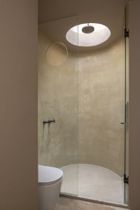 A minimalist bathroom featuring a concrete shower enclosure, circular skylight, and a white toilet.