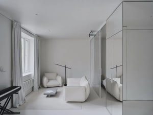 A minimalist living room with white furniture and walls, featuring a sofa, armchair, and small table.