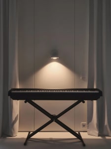 A minimalist music room featuring a black electronic keyboard on a stand, backlit by a wall-mounted light.