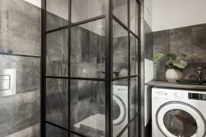 A modern laundry room featuring concrete walls and glass-enclosed shower stall.
