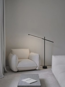 A modern living room with a concrete floor, a white armchair, a black floor lamp, and a granite table.