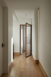 A minimalist corridor with wooden flooring, taupe-colored walls, and glass details.