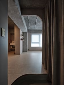 A minimalist residential space featuring exposed concrete walls and a large window.