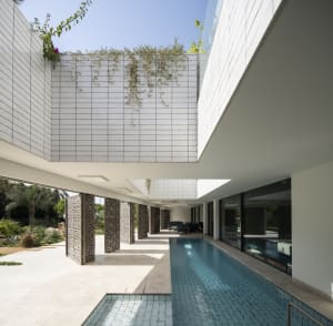 A modern residential house with concrete walls and a pool, featuring plants and a spacious interior.