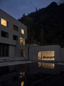 A modern residential interior with concrete walls and floors, featuring a large open space with a dining and seating area.