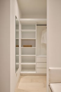 An organized closet with white wood shelves and drawers, showcasing a minimalist design.