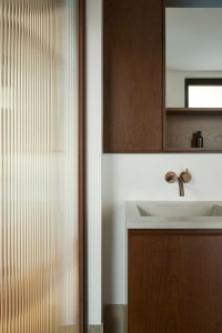 Modern minimalist bathroom featuring a wooden vanity, frosted glass wall panels, and a concrete sink with a metal faucet.
