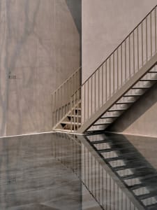 A concrete staircase with a metallic handrail reflected in a glossy floor.