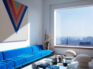 A living room with a blue sofa and a large window overlooking a cityscape.