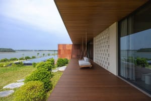 Modern residential terrace with wood floor, hanging swing, and concrete wall overlooking a lake.