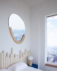 A minimalist bedroom featuring a fabric headboard and a view of a cityscape through a window.