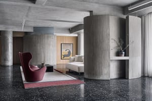 Modern living room with concrete and terrazzo flooring, featuring a red wingback chair and a beige sofa.