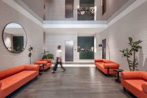 Modern, industrial-style lobby with brick walls, a green reception desk, and orange couches.