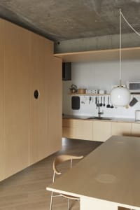 A modern kitchen with wooden cabinets, countertops, and flooring, featuring minimalist design elements and a concrete ceiling