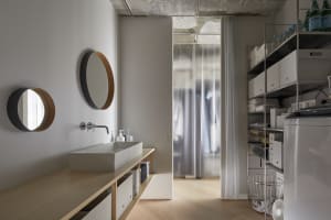 A minimalist laundry room with tall steel shelves, wood cabinetry, and a sink.