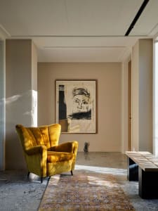 A modern interior design featuring a yellow upholstered armchair on a concrete floor, with a large abstract wall art piece.