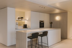 A modern minimalist kitchen with a white countertop and bar stools.