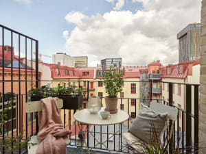 A small balcony with metal railing, potted plants, and a white table with a mug and vase.