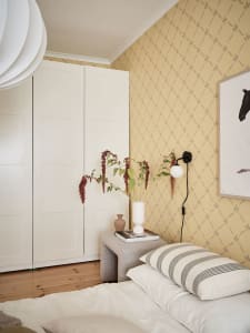 Minimalist bedroom with neutral tones featuring a bed, pillows, and a small bench with a white vase and flowers.