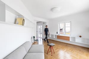 Minimalist living room with white walls, a gray sofa, and a wooden floor.