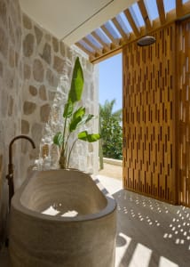 Modern minimalist bathroom featuring a stone bathtub and natural stone walls, framed by lush greenery.