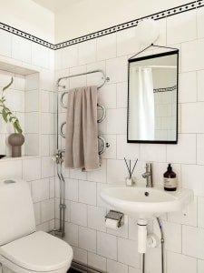 Minimalist bathroom with white tiled walls, white fixtures, and a gray towel hanging on a towel rack.
