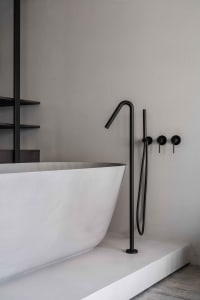 Modern minimalist bathroom featuring a freestanding concrete bathtub with matte black fixtures and a concrete floor.