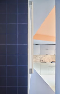 A minimalist kitchen featuring concrete walls and flooring, with a geometric design and white cabinets.
