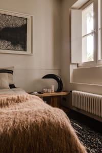 A minimalist bedroom featuring wooden furniture, a concrete headboard, and a wool blanket