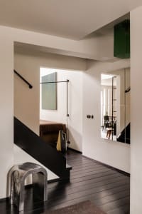 A minimalist interior with black stairs, white walls, and a black mirror on the wall.