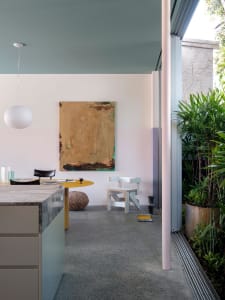 A minimalist residential kitchen with a concrete floor, concrete countertop, and a large abstract painting.