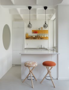 A minimalist kitchen with white cabinets, a white countertop, and colorful stools.